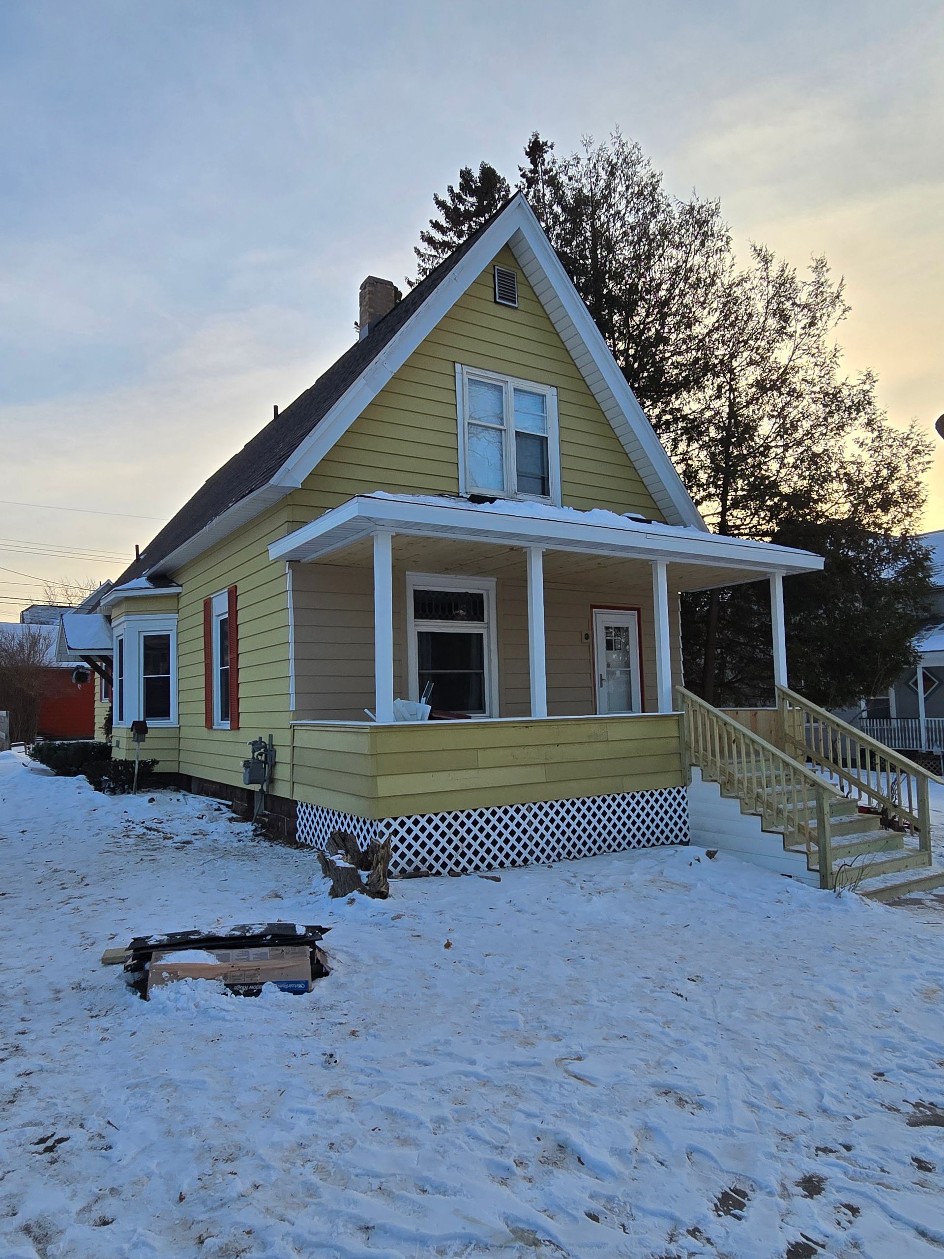 A yellow house with a porch and stairs in the snow