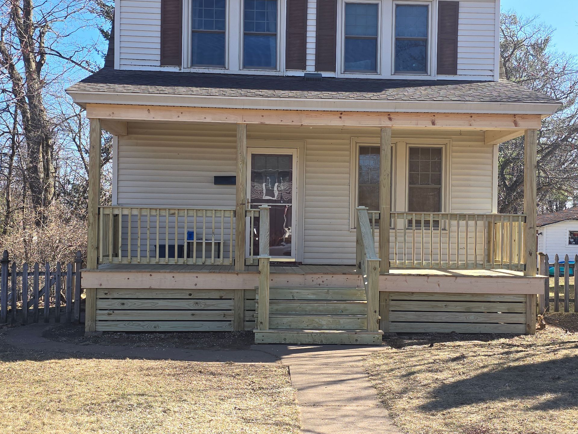 A white house with a wooden porch and a fence in front of it