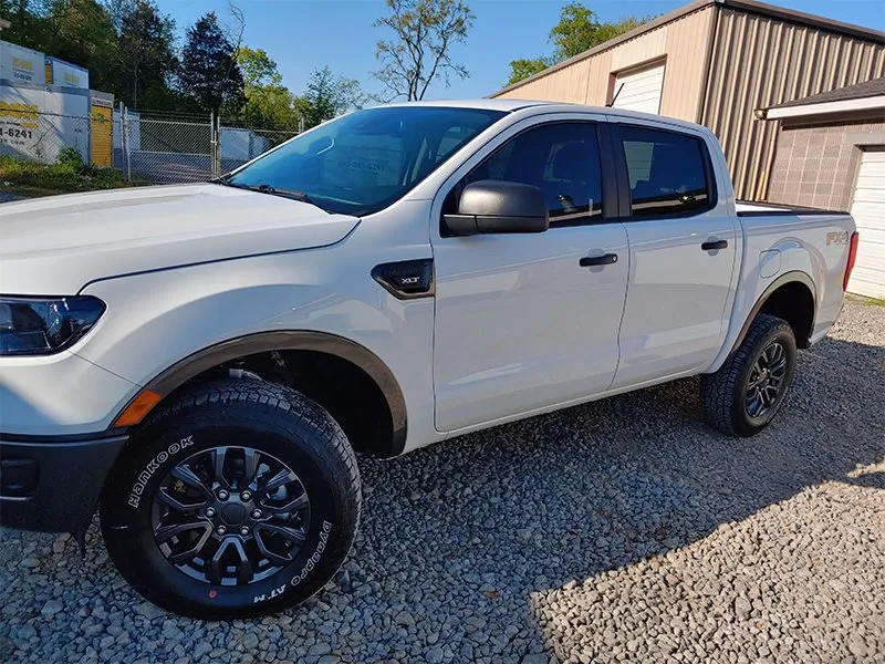 White Ford Ranger pickup truck with black wheels parked on gravel.