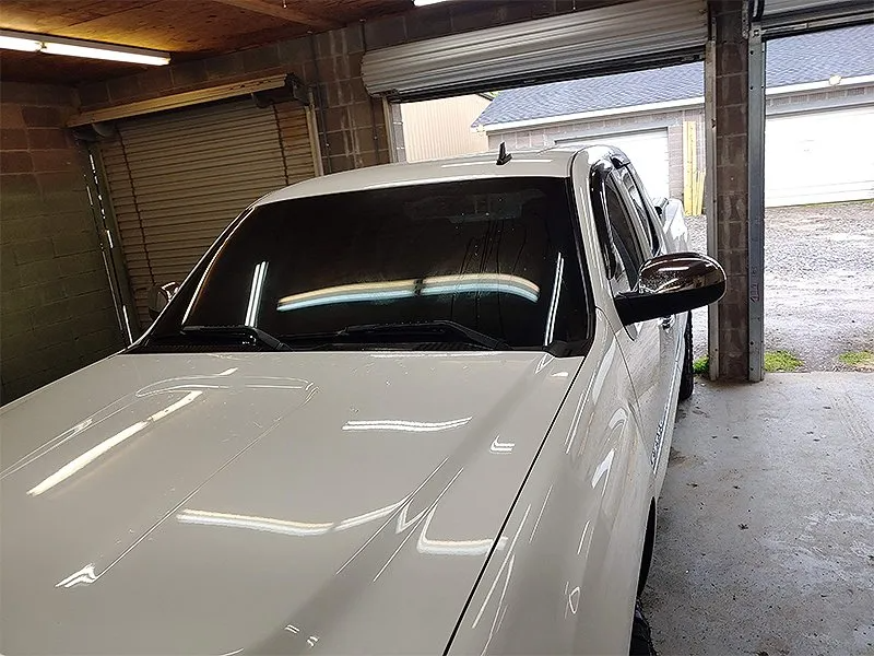 White pickup truck parked in garage, dark tinted windshield, shiny paint.