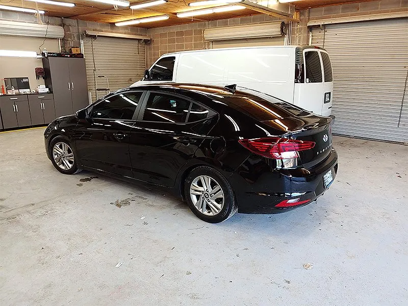 Black car parked in a garage with a white van in the background.