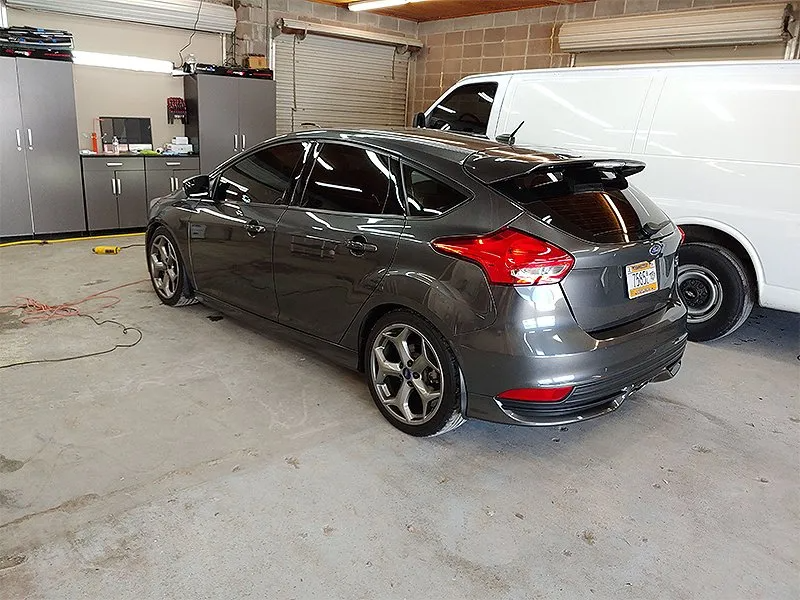 Gray Ford Focus hatchback parked inside a garage next to a white van.
