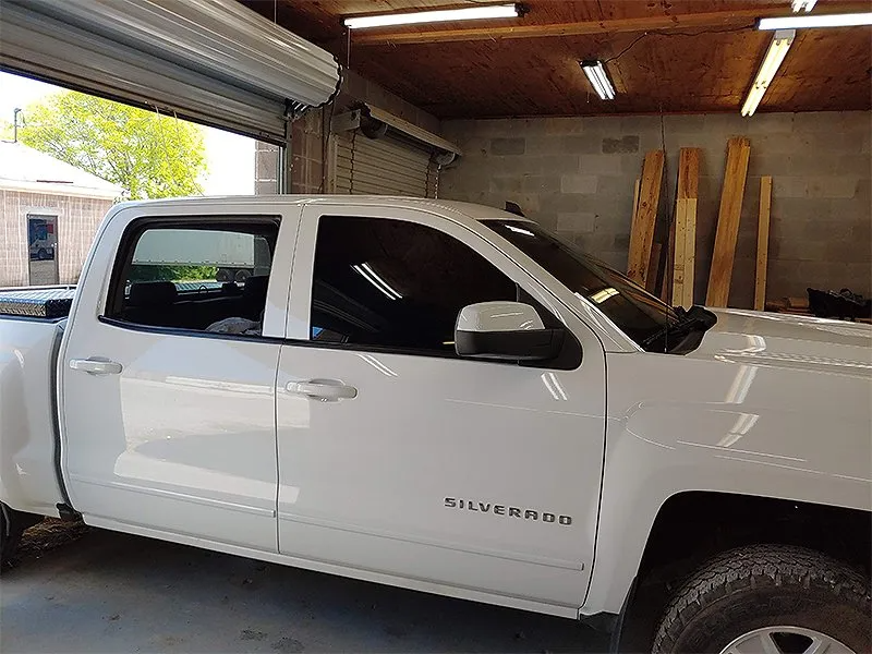 White pickup truck parked inside a garage with its windows tinted.