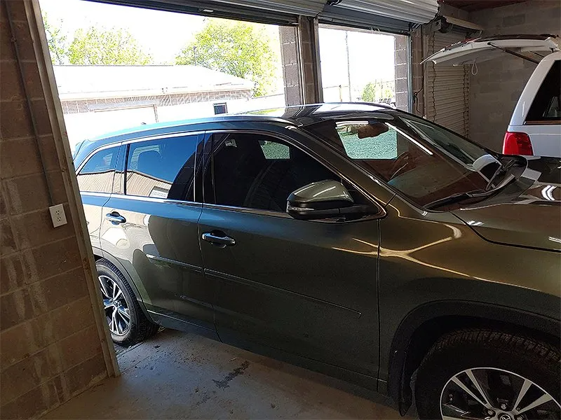 Green SUV parked inside a garage, with a white car visible on the right.