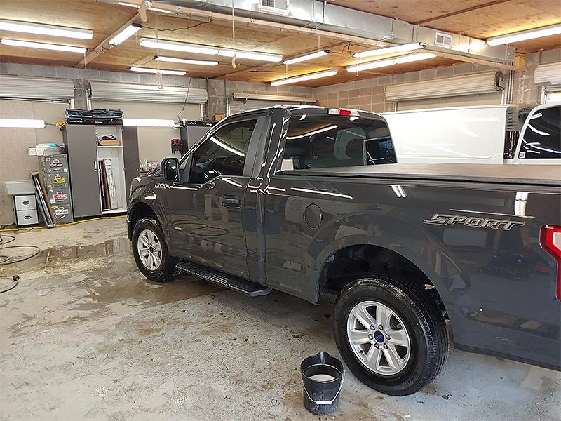 Dark gray Ford F-150 pickup truck in a garage, with a black bucket on the floor.