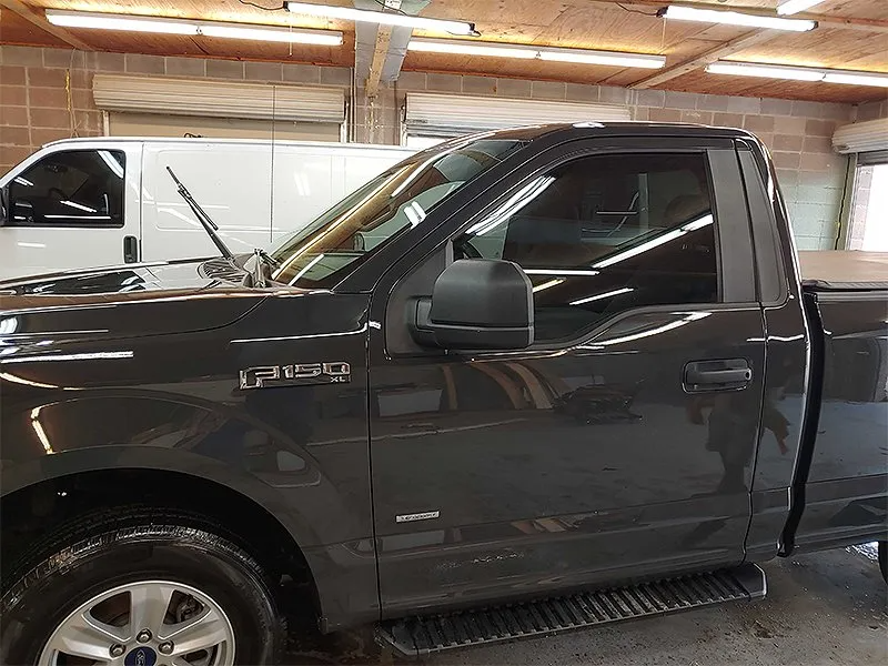 Dark gray Ford F-150 pickup truck parked indoors, next to a white van.