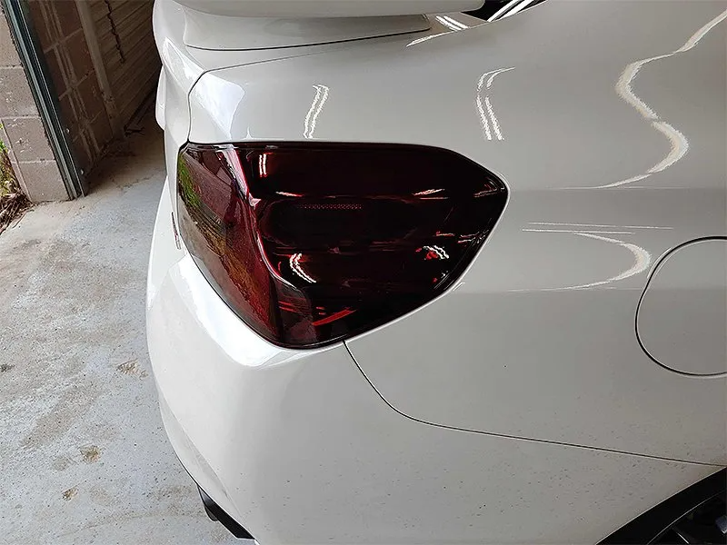 White car's rear with a tinted taillight, reflecting some surrounding greenery.