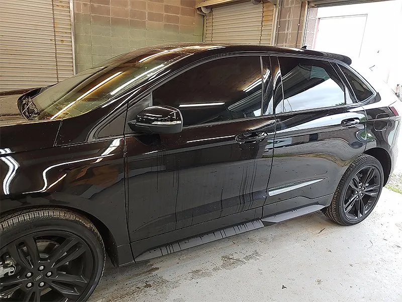 Black Ford Edge SUV with tinted windows parked inside a garage, black wheels and side steps.
