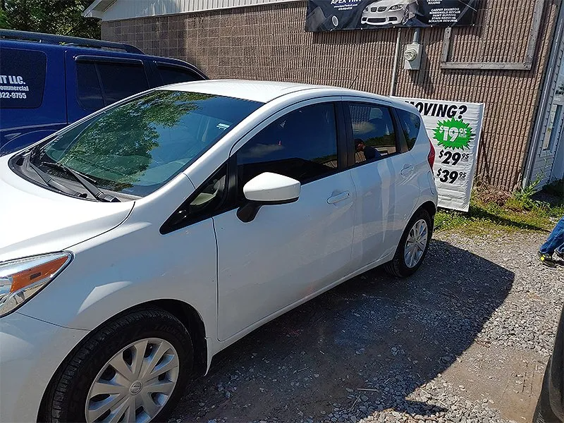 White hatchback car parked outside a business with a sign advertising tinting services.