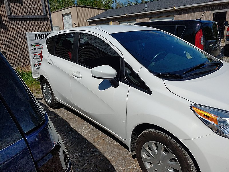 White Nissan hatchback parked outdoors, sunny day.