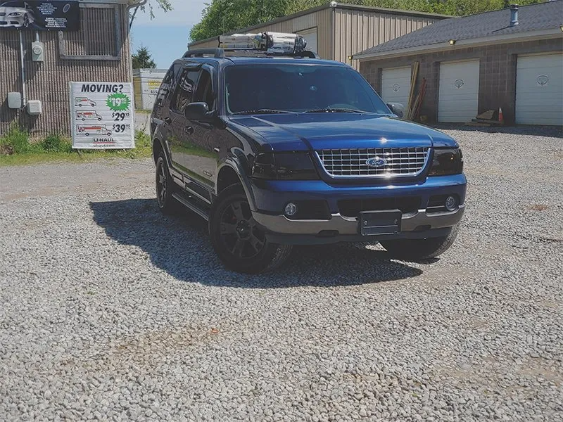 Blue SUV parked on gravel, with tinted windows, black rims, in front of a garage and storefront.