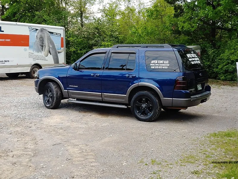 Blue SUV parked on gravel, with black rims, next to a moving truck.