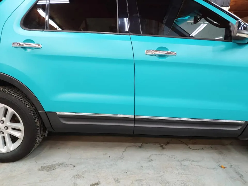 Teal SUV parked indoors with chrome door handles and trim, black lower body, and silver wheels.