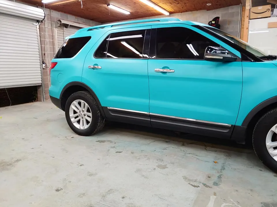 A teal SUV parked in a garage with a partially open garage door and a wooden ceiling.