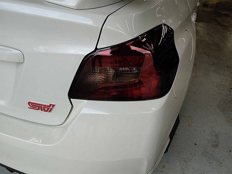 White car's rear with a tinted taillight, a red STI emblem, in a garage setting.