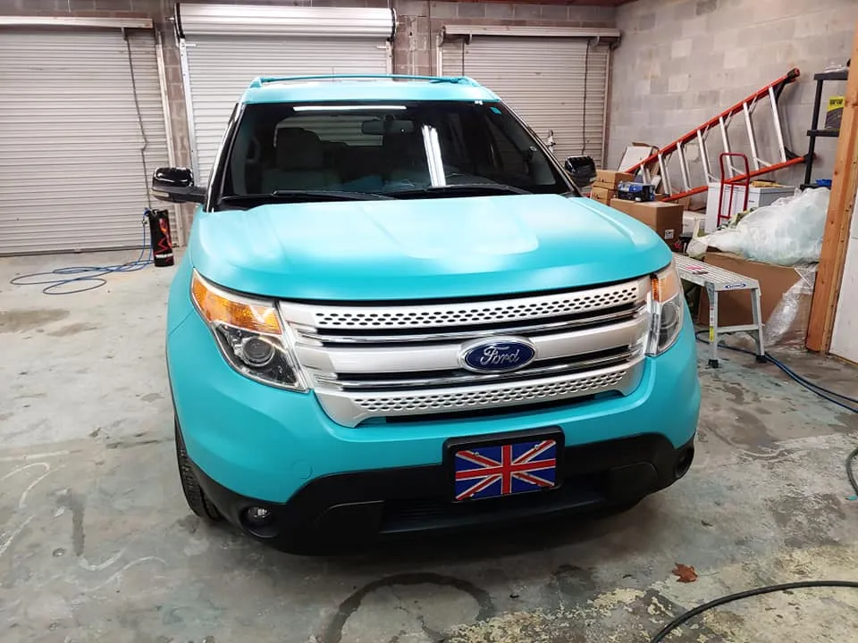 A teal Ford Explorer with a Union Jack license plate parked in a garage.