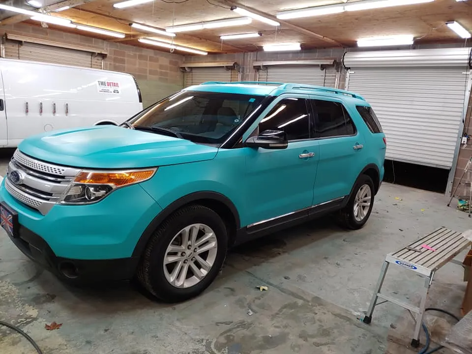Turquoise Ford Explorer in a garage, with a white van in the background.