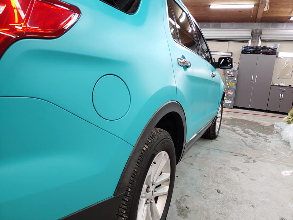 A teal SUV, with matte finish, parked indoors.