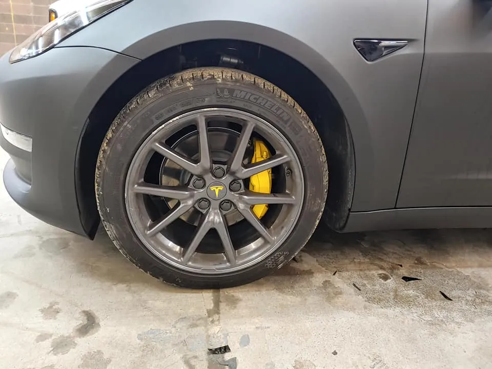 Close-up of a matte gray Tesla car wheel with a gray rim and yellow brake caliper.