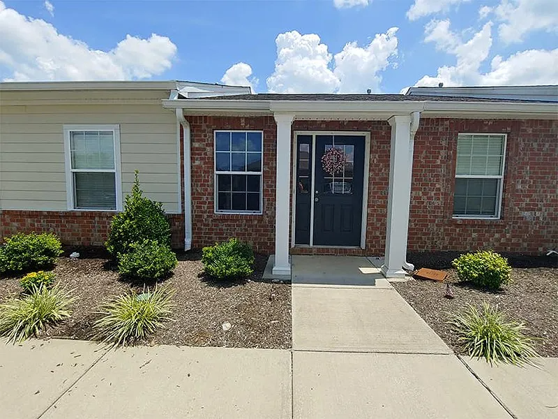 Exterior view of a brick building with a dark front door under a covered porch and landscaping.