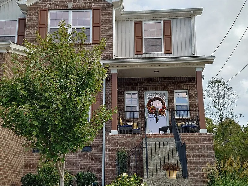 Two-story brick house with a porch, brown shutters, and a wreath on the front door.