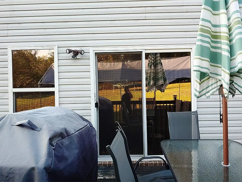 Back patio with a covered grill, sliding door, and umbrella. A person's reflection is seen in the glass.