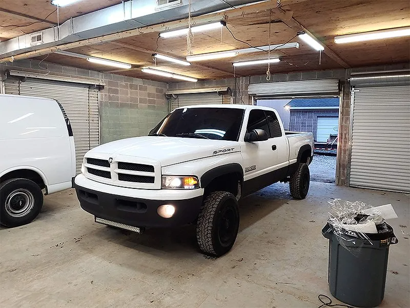 White Dodge Ram truck in a garage, parked in front of roll-up doors.