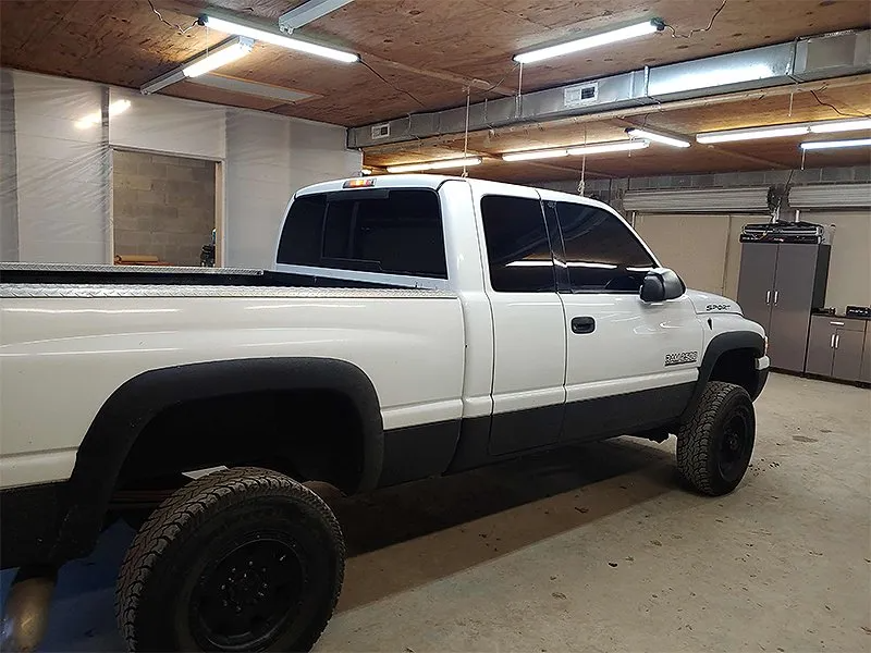 White Dodge Ram pickup truck in a garage, black tires and trim.