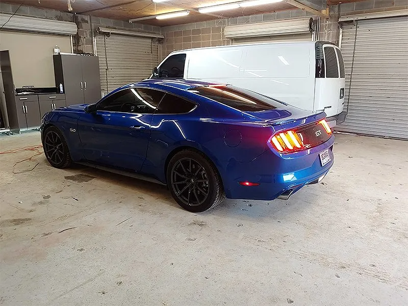 Blue Ford Mustang in a garage, white van in the background, next to cabinets.