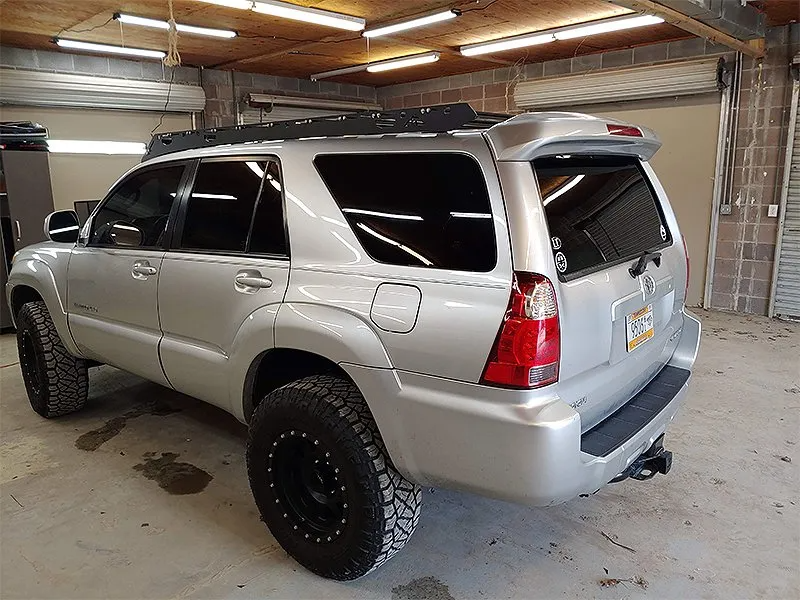 Silver SUV with black tinted windows, roof rack, and off-road tires, parked in a garage.