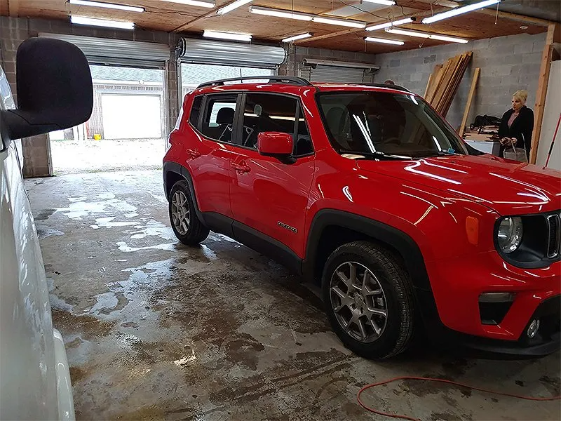 Red Jeep Renegade parked in a garage. A person stands in the background near wood beams.