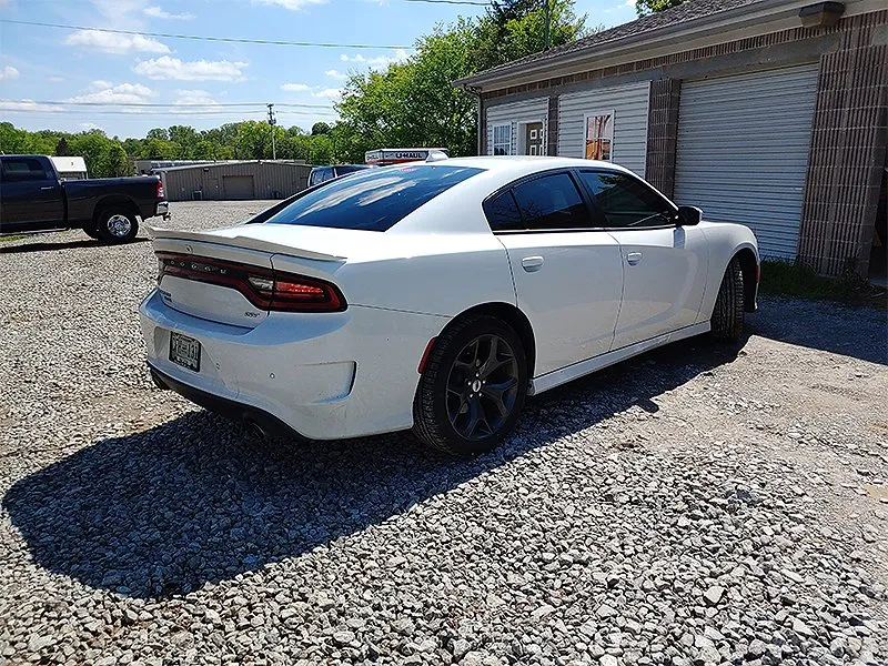 White Dodge Charger parked on gravel in front of a building on a sunny day.