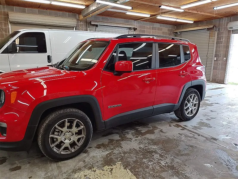 Red Jeep Renegade parked inside a garage. White van is partly visible in the background.