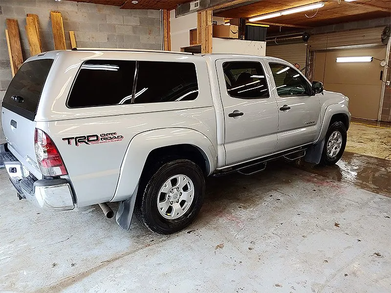 Silver Toyota Tacoma truck with a camper shell in a garage.