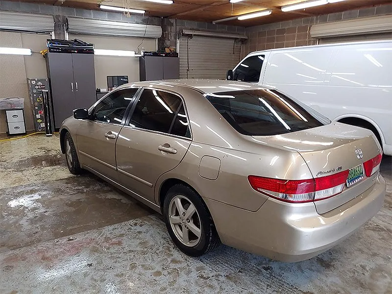 Gold Honda Accord parked in a garage with a white van and storage cabinets in the background.