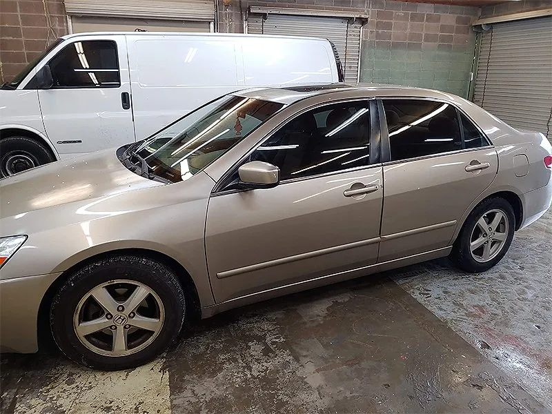 Gold Honda Accord sedan parked indoors with a white van in the background.