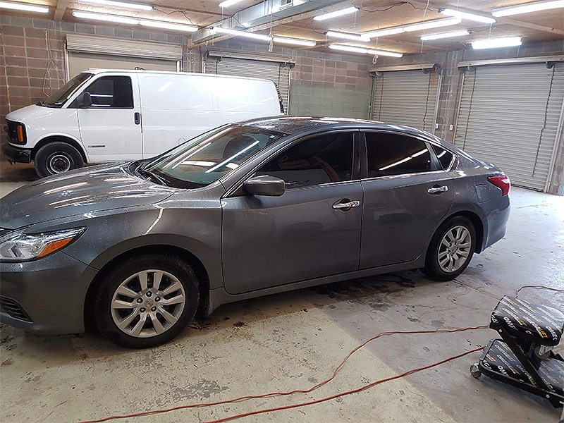 Gray sedan parked inside a garage next to a white van, ready for tinting.