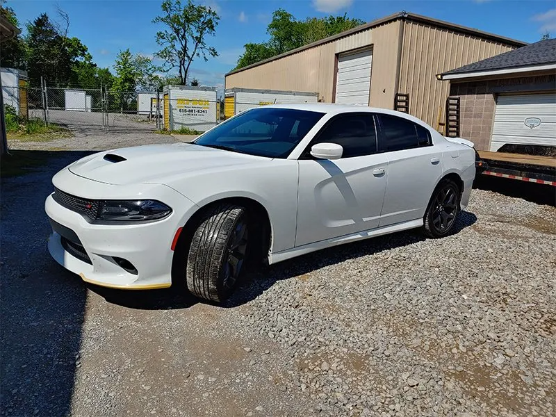 White Dodge Charger parked on gravel in front of a building on a sunny day.