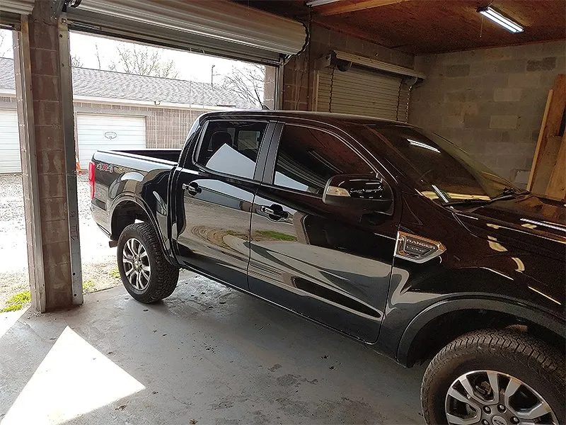 Black pickup truck in a garage, with a partially open roll-up door.