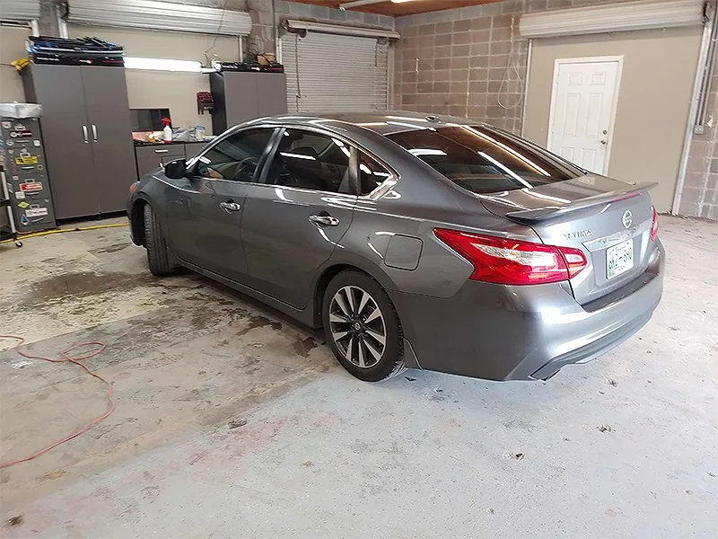 Gray sedan parked in a garage with tools and cabinets in the background.