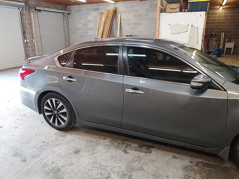 Gray sedan parked in a garage with tinted windows, set against a brick wall.