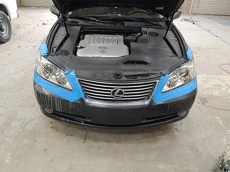 Black Lexus car with open hood; bumper taped for painting.