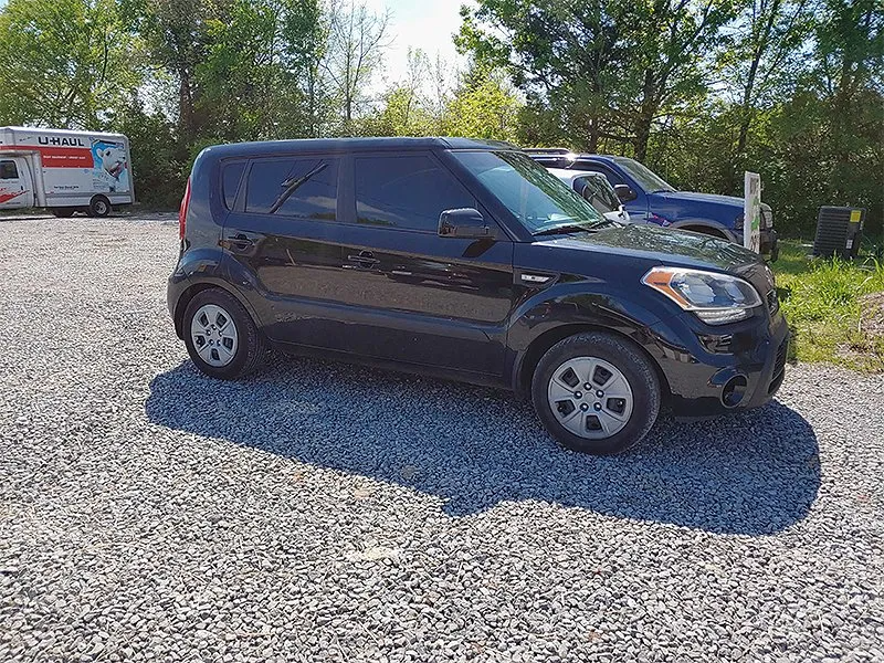 Black Kia Soul parked on gravel. A U-Haul truck and another vehicle are in the background.