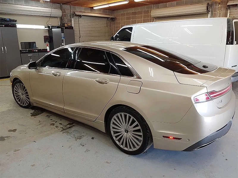 Tan Lincoln MKZ sedan parked inside a garage, windows tinted, near a white van.