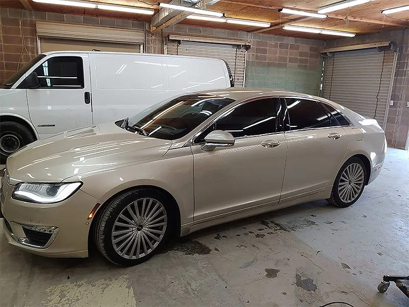 Tan Lincoln MKZ sedan with tinted windows inside a garage, beside a white van.