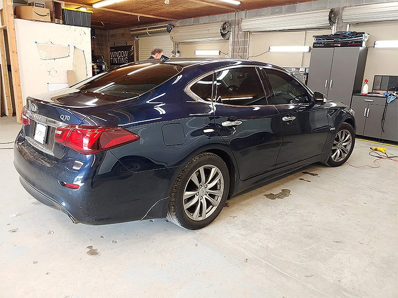 Dark blue Infiniti sedan in a garage, tinted windows, person visible.