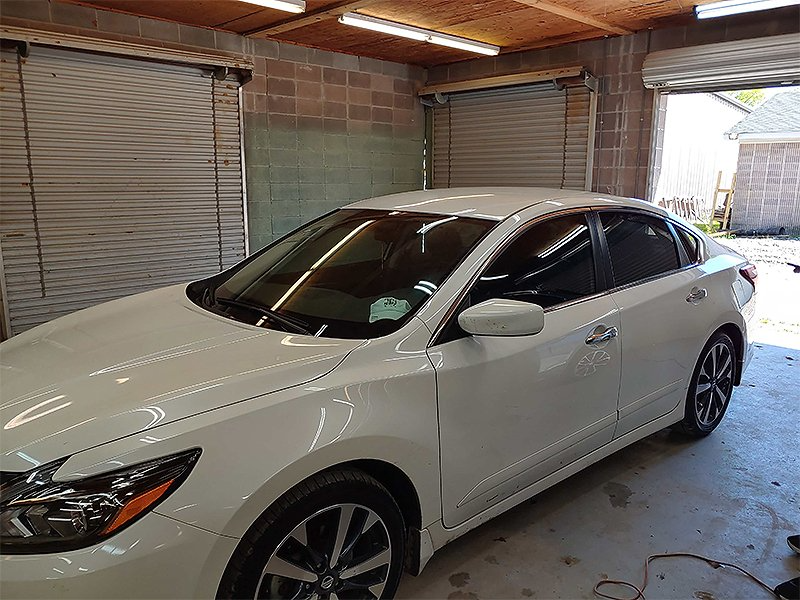 White Nissan Altima in a garage with tinted windows.