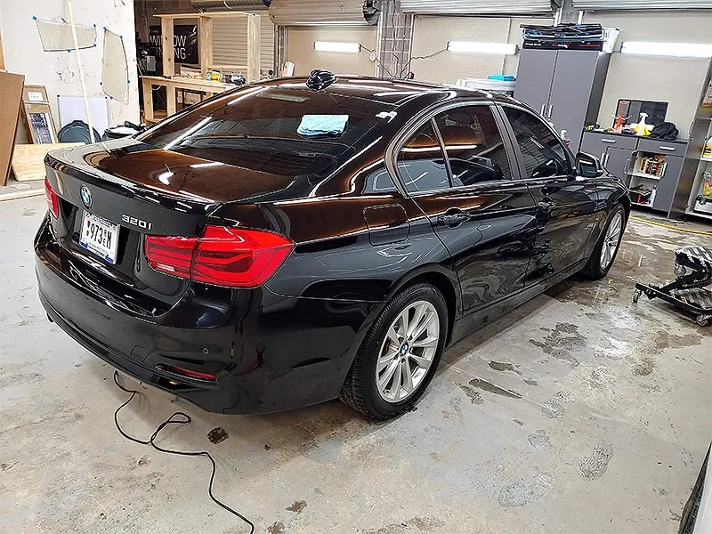 Black BMW sedan in a workshop, windows tinted, parked on a concrete floor.
