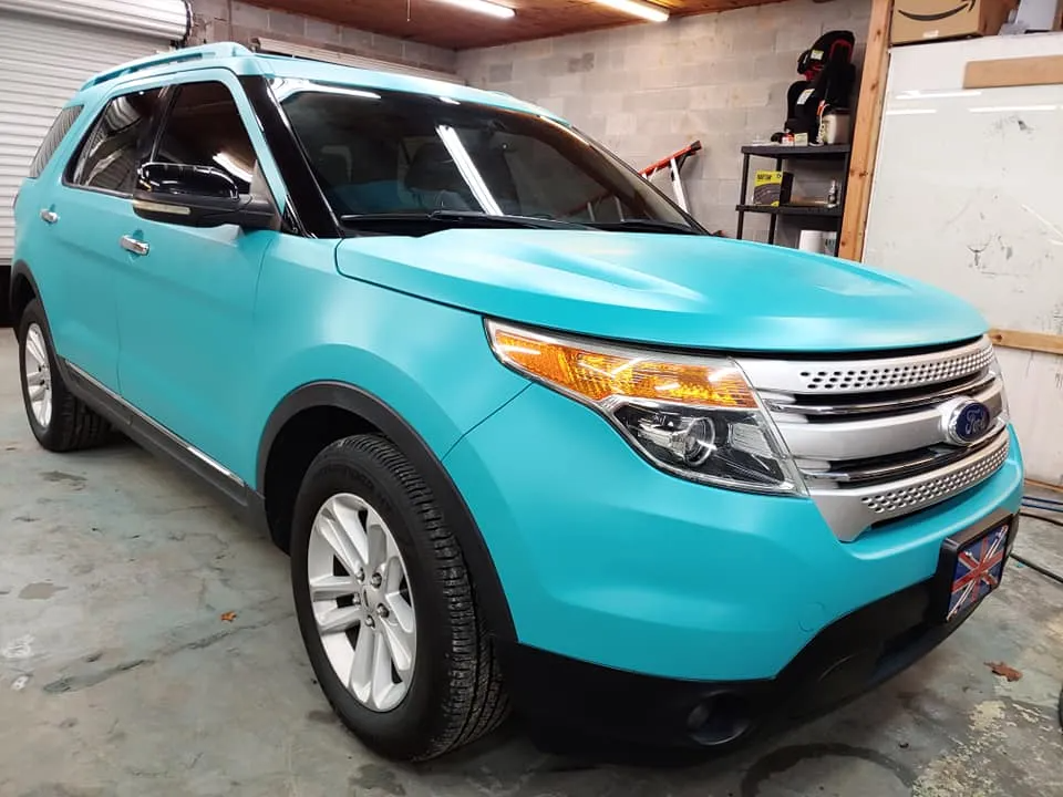 A teal Ford Explorer in a garage with black trim, silver grill, and headlights.