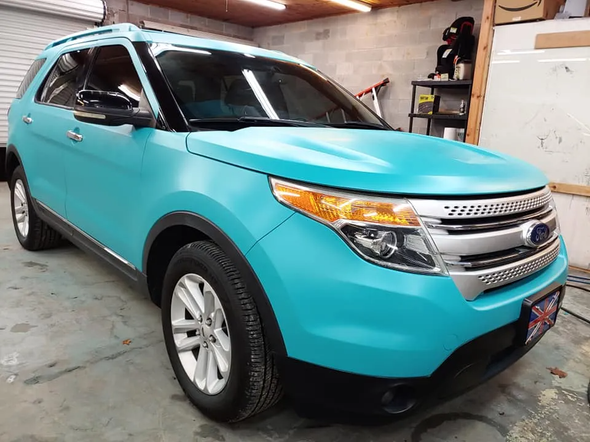 A teal Ford Explorer in a garage with black trim, silver grill, and headlights.